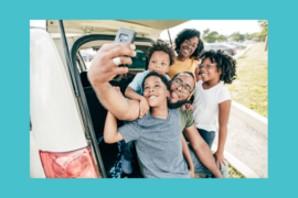 A Black family of 5 people takes a selfie photo from the trunk of the car. The tailgate is lifted.
