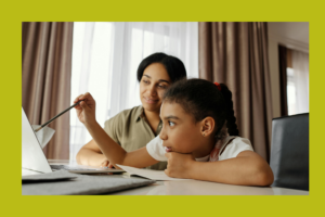 A parent and child are seated together in front of a computer monitor.