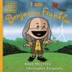 The cover of the book I Am Benjamin Franklin by Brad Meltzer, illustrated by Christopher Eliopoulos. The illustration features a cartoon depiction of Benjamin Franklin holding a kite with a key attached, standing on a grassy field with trees in the background. Lightning strikes in the sky behind him. The title is written in yellow, and the top left corner displays the series name, 'Ordinary People Change the World.