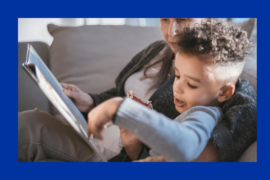 A woman and small child are seated on a sofa. The child is pointing to a page in the book they are reading together.