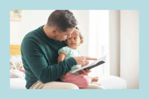 Father reading a book to his toddler daughter while sitting on a bed in a bright room, fostering early literacy and bonding.