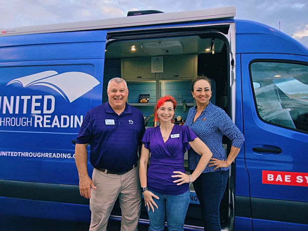 United Through Reading staff and volunteers standing in front of a blue mobile reading van.
