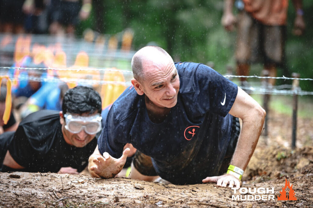 Man crawls through mud during charity Tough Mudder run.