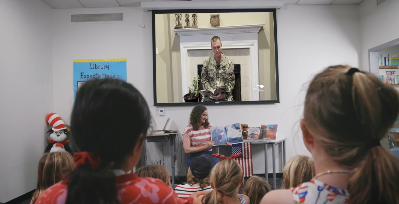 Classroom of students watching a service member reading stories on a big screen