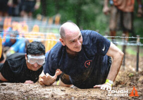 Man crawls through mud during charity Tough Mudder run.