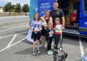 Military family holding books in front of United Through Reading van