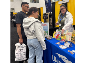 Woman behind a table topped with books. She is speaking to a military couple.