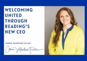 Graphic announcing United Through Reading’s new CEO. On the left, blue text reads “Welcoming United Through Reading’s New CEO” with the name “Carrie Valentine Fuller” and a handwritten signature below. On the right is a portrait of a smiling woman with long wavy brown hair, wearing a bright yellow cardigan over a blue top, standing against a neutral background. The design features a bold royal-blue border.