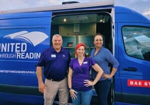 United Through Reading staff and volunteers standing in front of a blue mobile reading van.